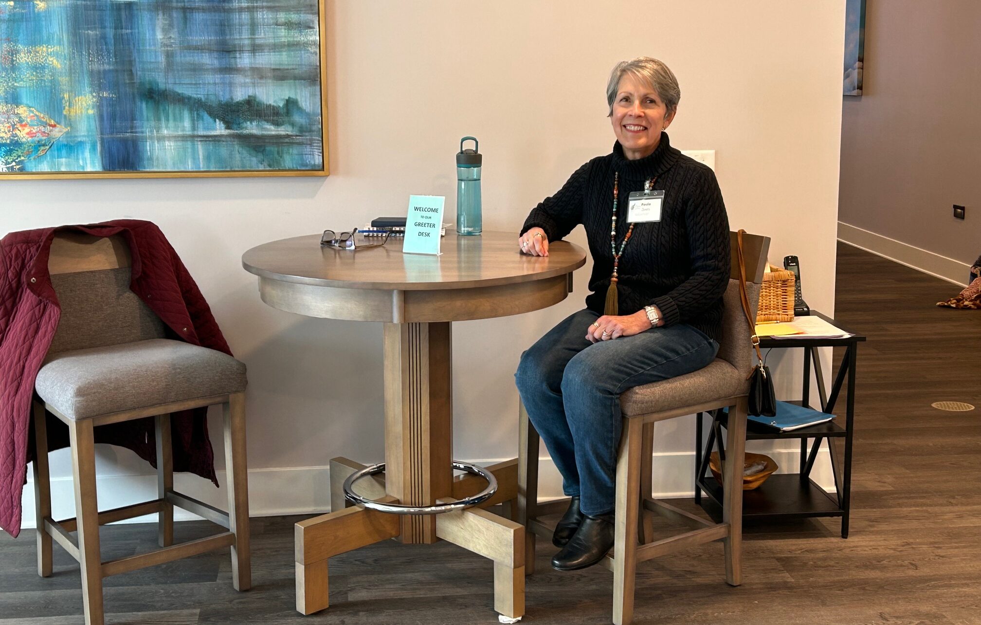 A woman sitting on a high chair at a small desk.