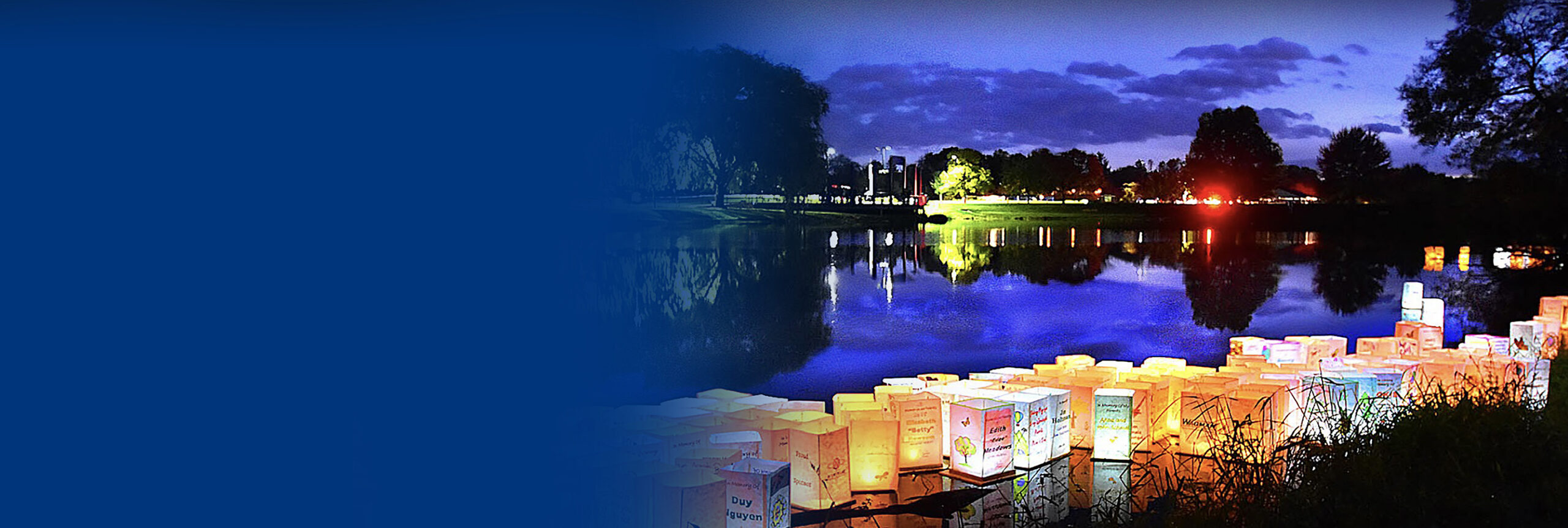 A view across a small lake at dusk with lit up paper lanterns floating across the lake.