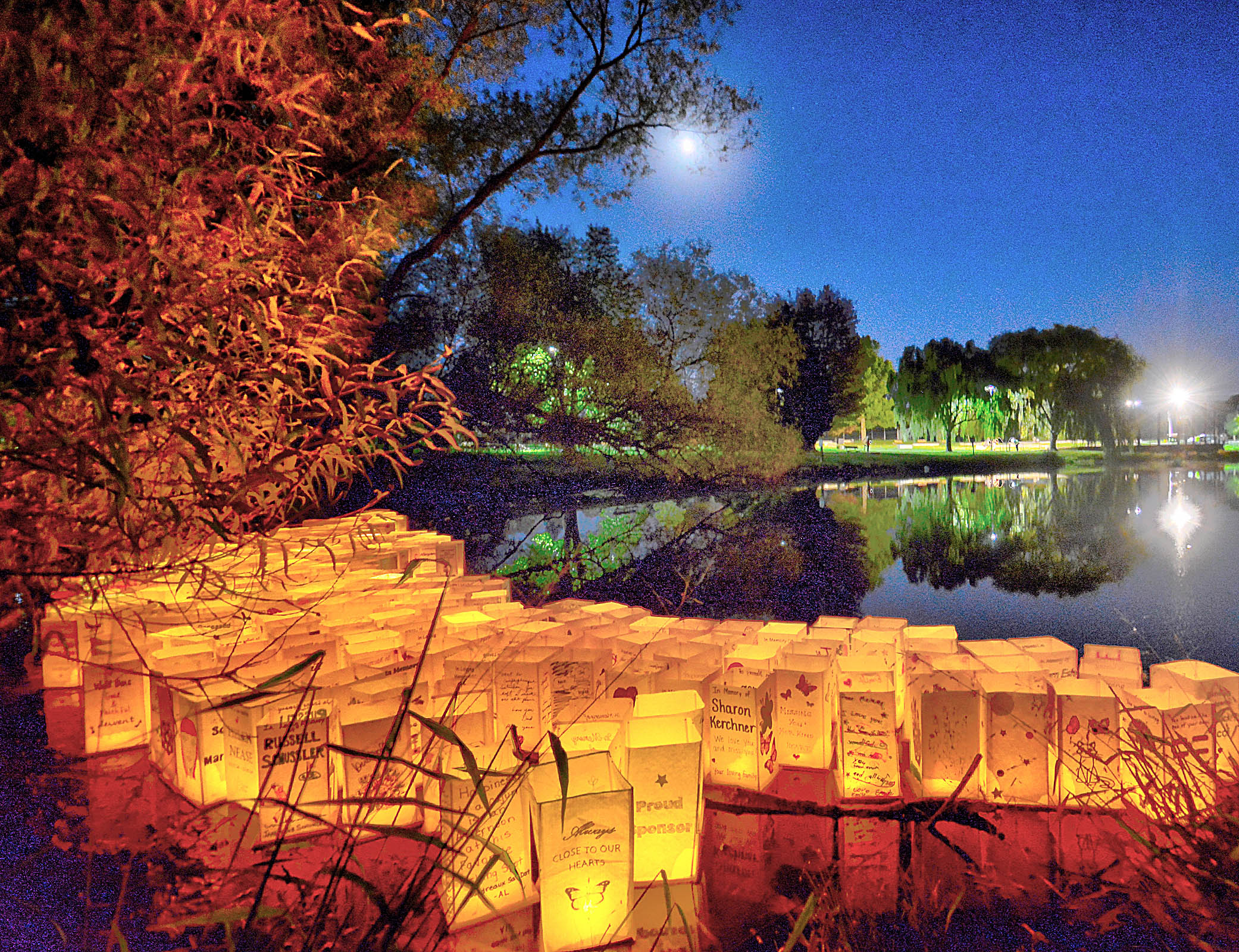 A view across a small lake at dusk with lit up paper lanterns floating across the lake.